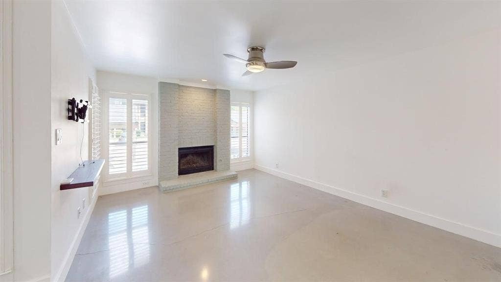 Living area featuring polished concrete flooring, a floor-to-ceiling painted brick fireplace, a built-in wall-mounted shelf, plantation shutters, and a central ceiling fan