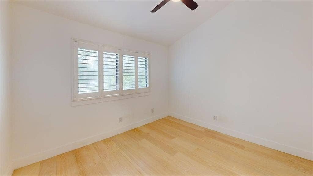 Room featuring vaulted ceilings, wood-finish flooring, and white plantation shutters, complemented by a ceiling fan