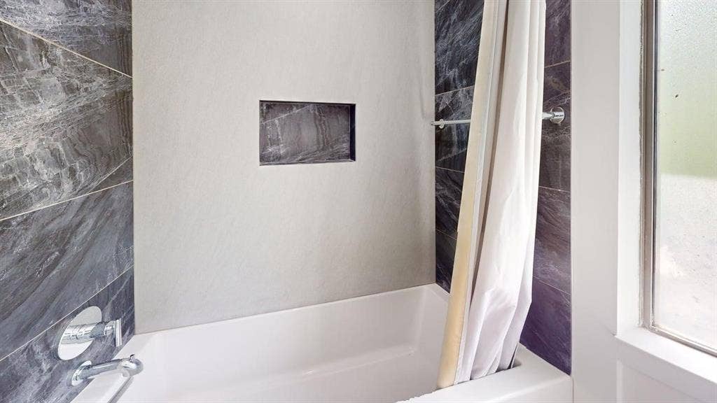 Bathtub with polished chrome fixtures, integrated wall niche, and contrasting large-format dark stone-finish and neutral-tone tile surrounds