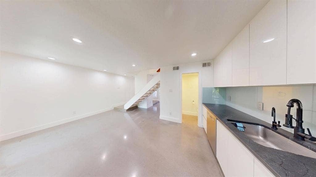Kitchen featuring high-gloss cabinetry, dark stone countertops, a glass backsplash, and an undermount stainless steel sink with a matte black faucet