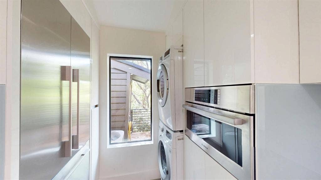 High-gloss cabinetry, floor-to-ceiling built-in refrigerator, stacked laundry unit, stainless steel oven, and window