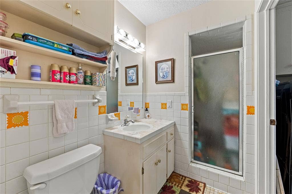 Bathroom featuring tiled walls with decorative accents, a walk-in shower with a glass door, a built-in cabinet with a tile-topped vanity, and wall-mounted shelving