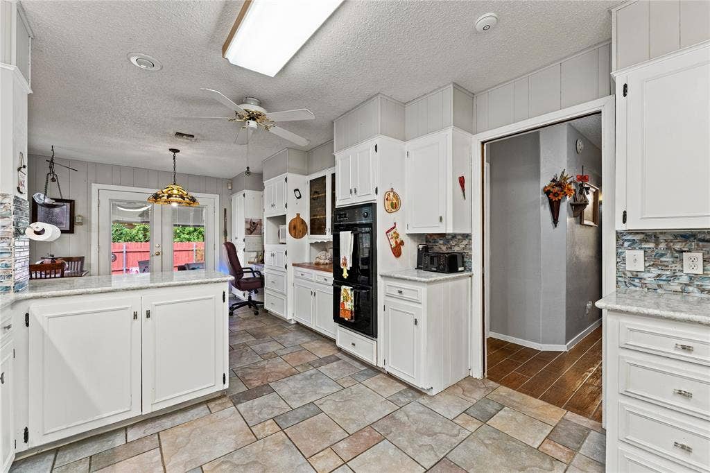 Kitchen featuring white cabinetry, stone-finish countertops, built-in double ovens, multi-toned tile flooring, and glass-paned double doors