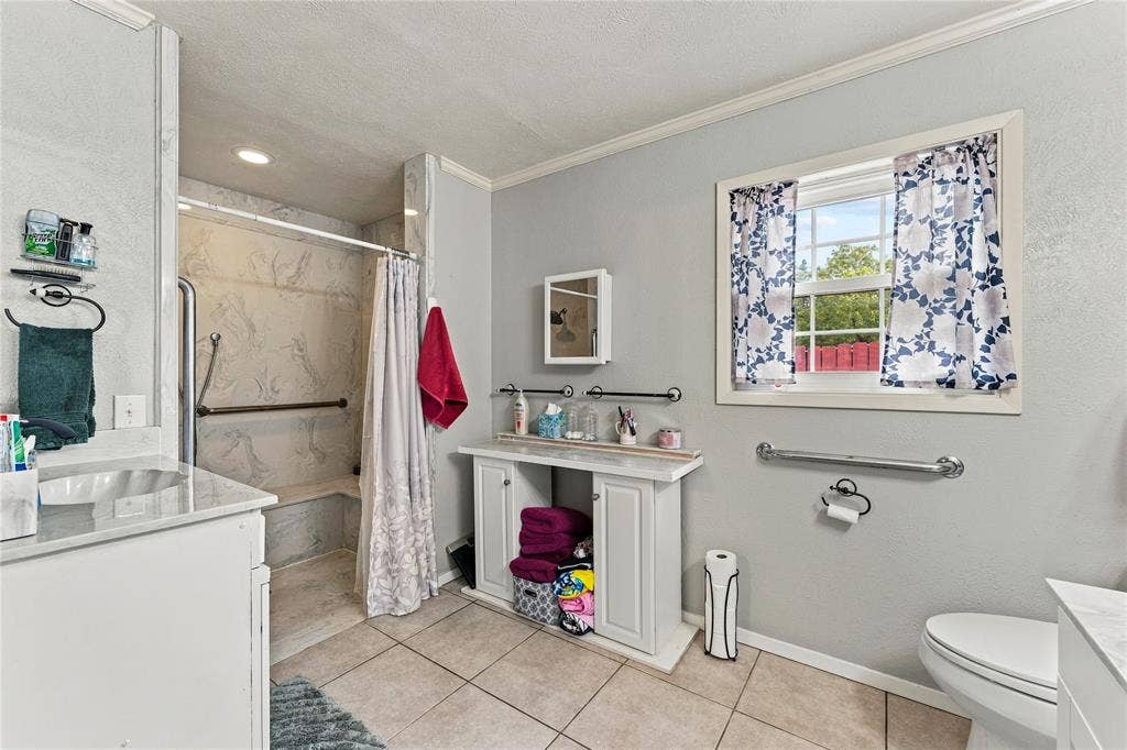 Bathroom featuring tile flooring, a walk-in shower with integrated seating, white cabinetry, a single-basin vanity with stone-finish countertop, and a window with white trim