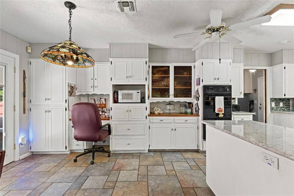 Kitchen featuring white cabinetry, built-in wall oven, multi-patterned stone-finish flooring, decorative pendant lighting, and a multi-level island with stone-finish countertop
