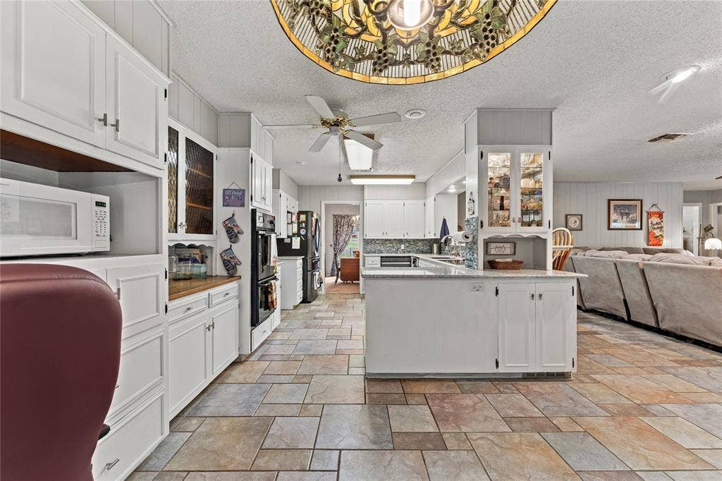 Kitchen featuring white cabinetry with glass-front display uppers, built-in wall oven, multi-tonal ceramic tile flooring, and decorative stained-glass pendant lighting
