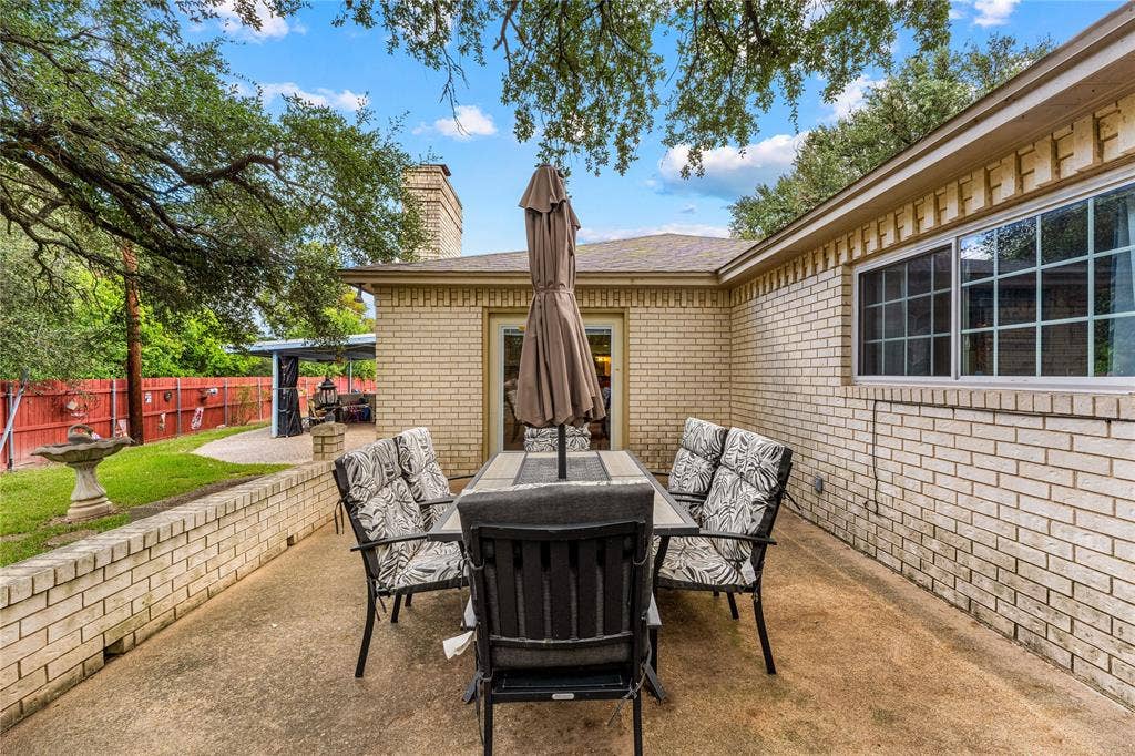Exterior patio featuring brick masonry construction, a concrete foundation, a low-profile brick retaining wall, and mature tree canopy