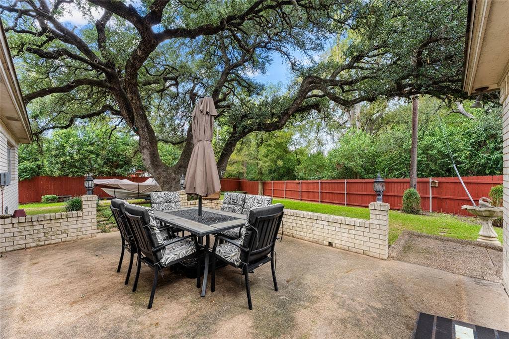 Concrete patio featuring a low-profile brick retaining wall and mature canopy trees