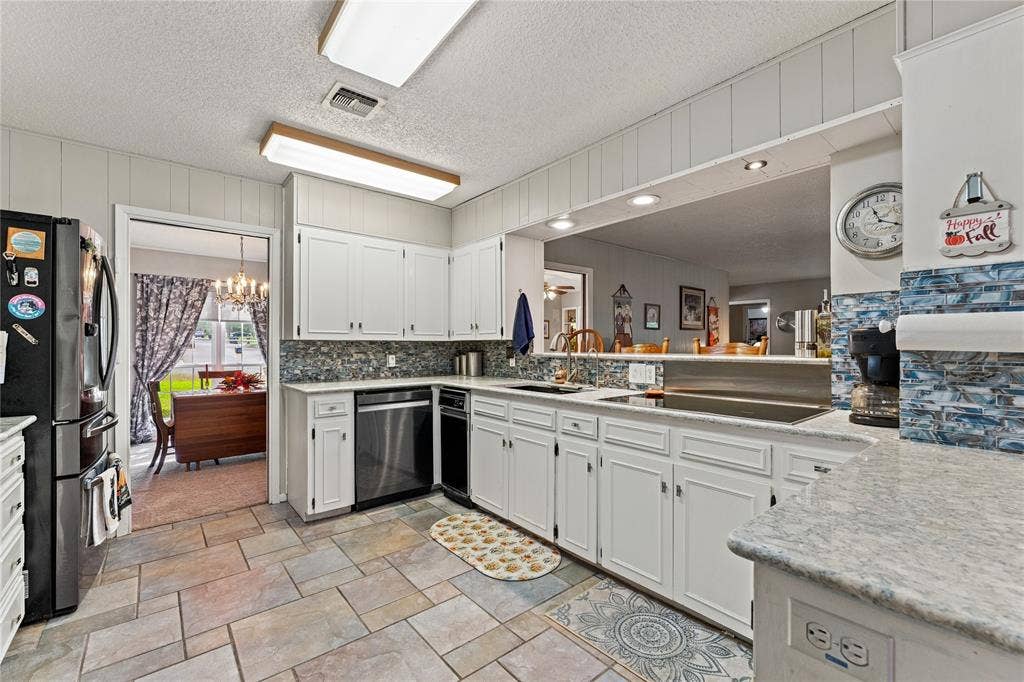 Kitchen featuring white cabinetry, stone-finish countertops, decorative tile backsplash, built-in stainless steel dishwasher, and tiled flooring