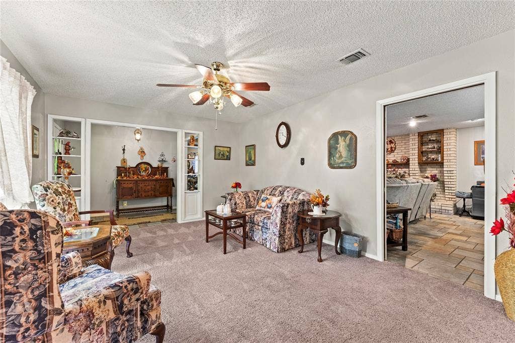 Living area featuring dual built-in display shelving, textured ceiling, central ceiling fan with integrated lighting, and neutral wall tones
