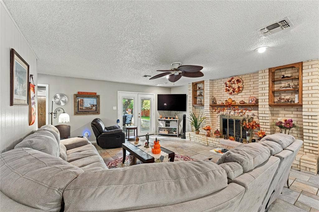 Living area featuring a floor-to-ceiling brick fireplace with a wood mantel, built-in shelving, stone-finish flooring, and double-glass doors