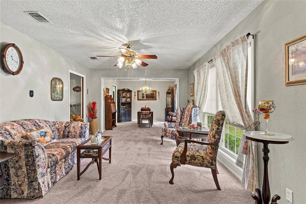 Living area featuring neutral wall tones, multi-light ceiling fan, and large windows with integrated window treatments