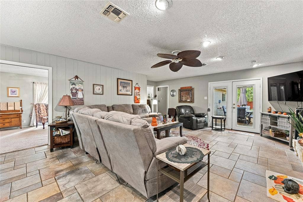 Living area featuring large-format tile flooring, a ceiling fan with integrated lighting, and glass-paned double doors