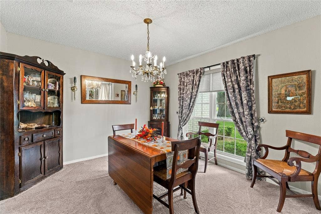 Dining area featuring a central candle-style chandelier, large window with natural light, and neutral wall tones