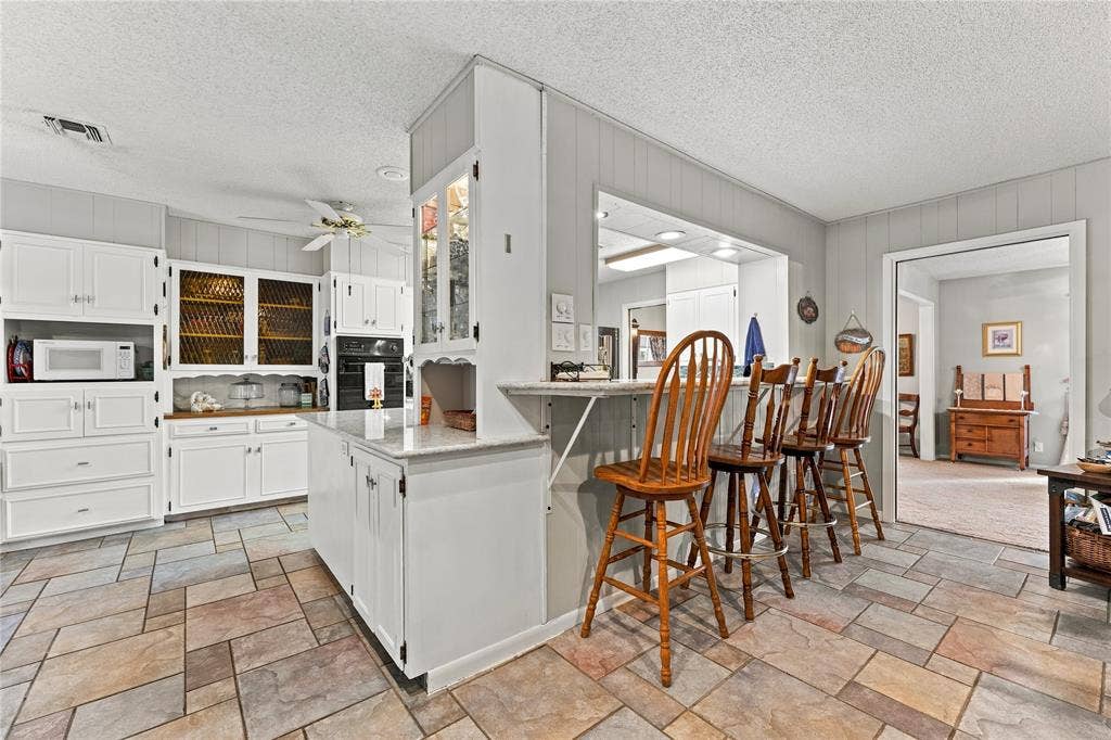 Kitchen featuring custom white cabinetry, stone-finish countertops, multi-toned tile flooring, built-in display hutch, and breakfast bar seating