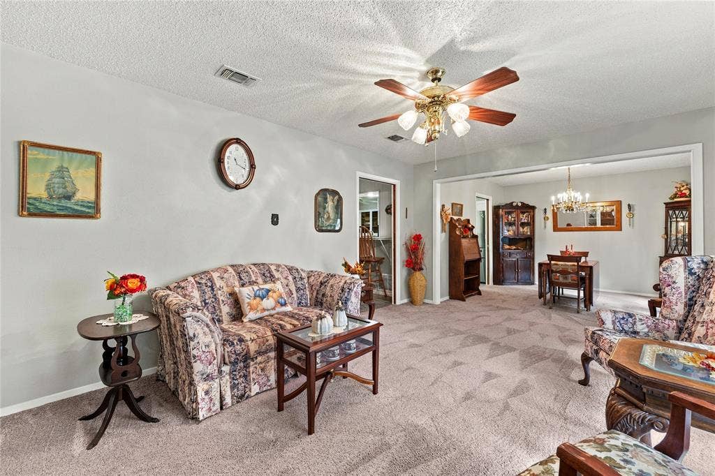 Living area featuring wall-to-wall carpeting, textured ceiling, ceiling-mounted fan with integrated lighting, and crown molding