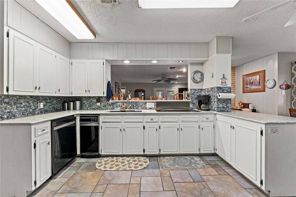 Kitchen featuring white cabinetry, stone-finish countertops, mosaic tile backsplash, large-format tile flooring, and integrated black dishwasher and cooktop