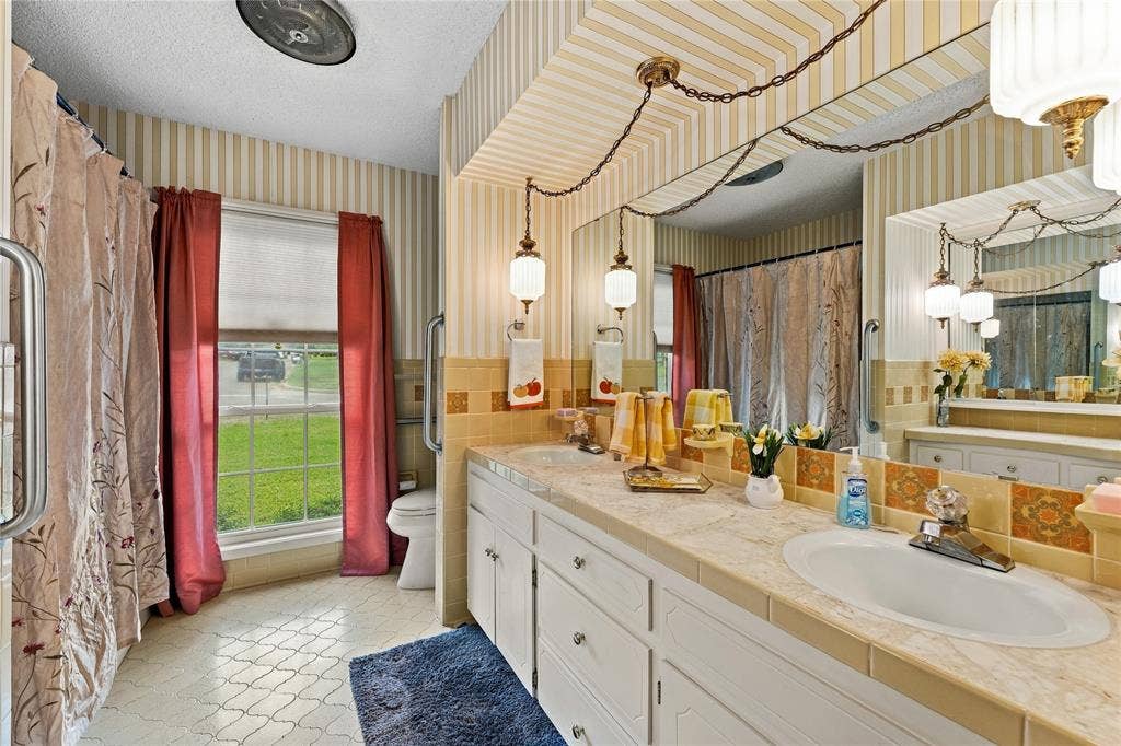 Double vanity featuring stone-finish countertops, undermount sinks, patterned tile backsplash, and decorative pendant lighting