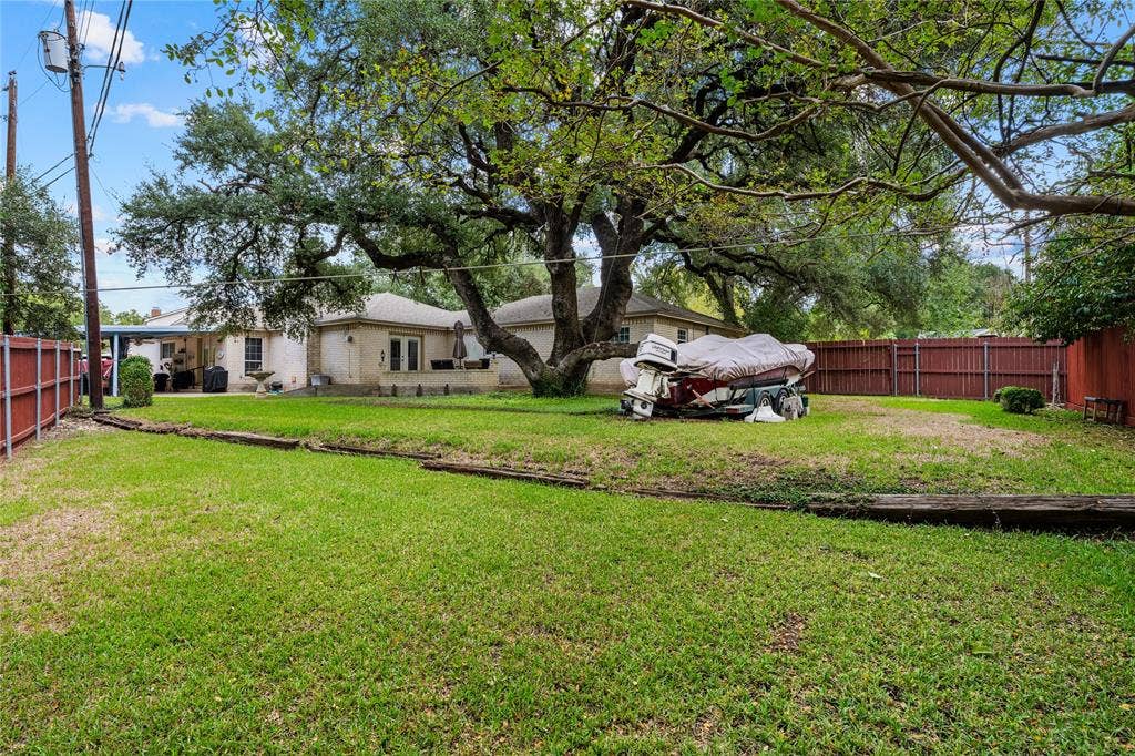 Spacious backyard featuring a large mature tree, wood-finish privacy fencing, and timber landscape edging