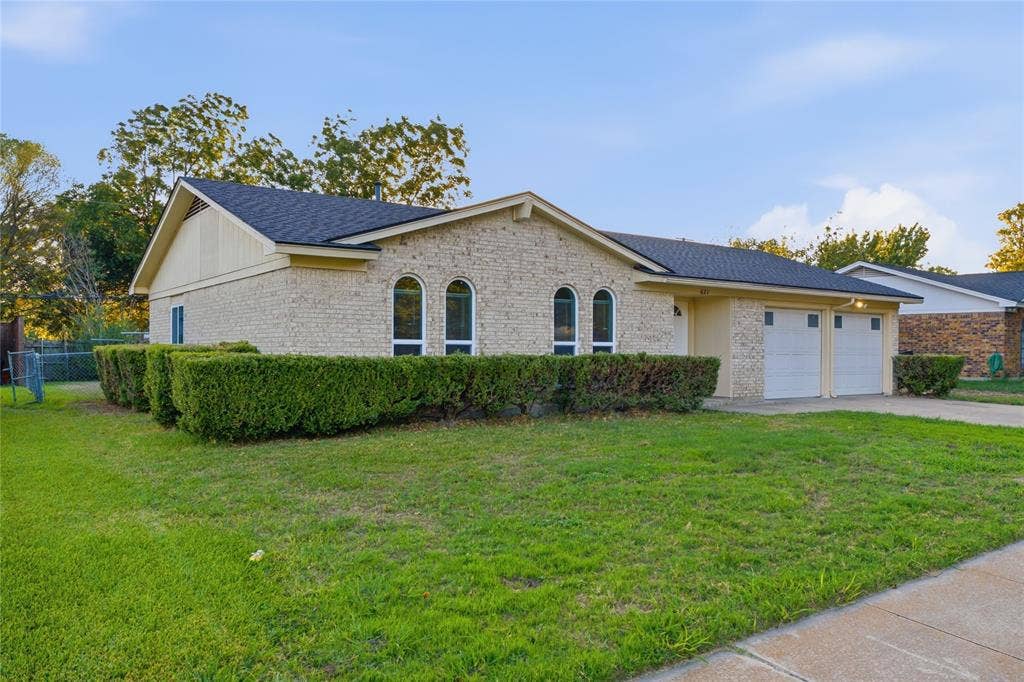 Single-story residence featuring a light-toned brick facade, arched window detailing, dark shingle roofing, and an attached two-car garage