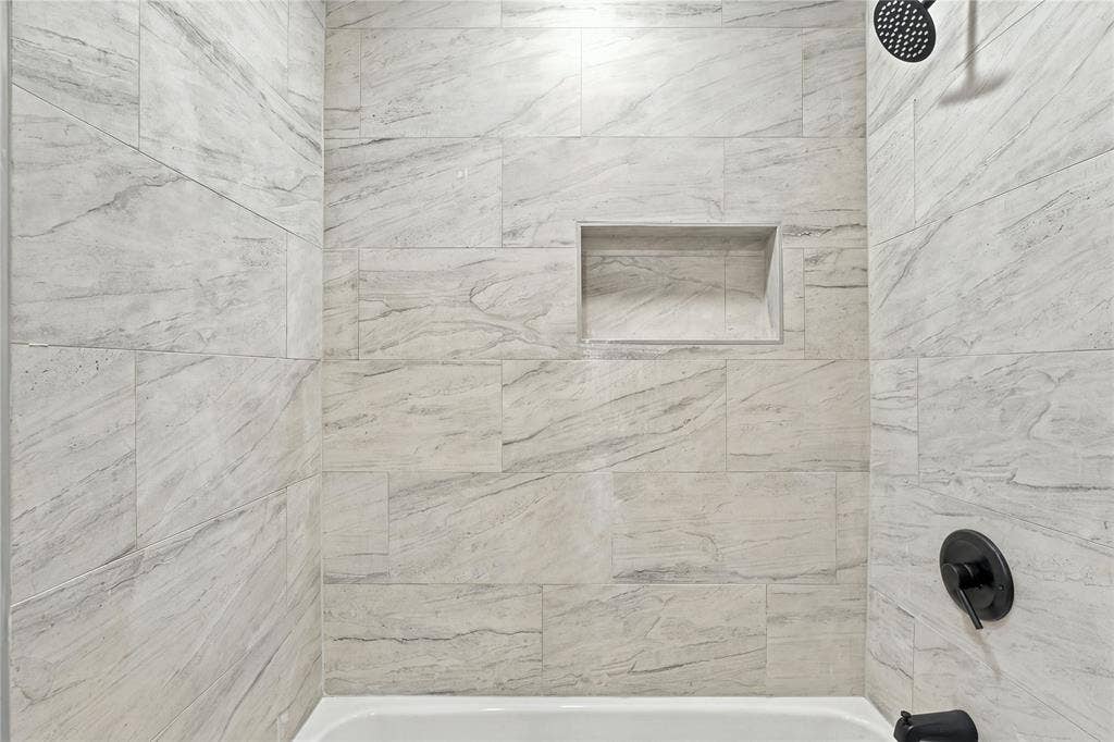 Shower enclosure featuring large-format neutral-toned tile, recessed wall niche, and matte black plumbing fixtures
