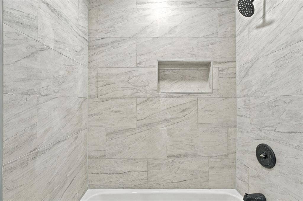Shower enclosure featuring large-format stone-patterned wall tile, built-in recessed wall niche, matte black rainfall showerhead, and matching matte black control fixture