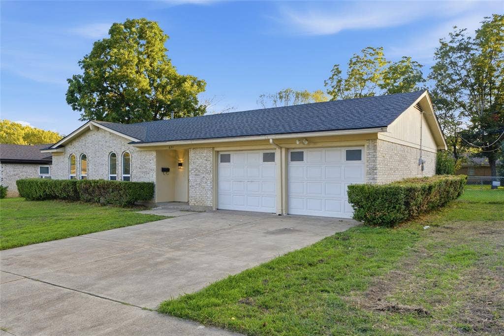 Single-story residence featuring light-colored brick siding, an attached two-car garage, arched window detailing, and a concrete driveway