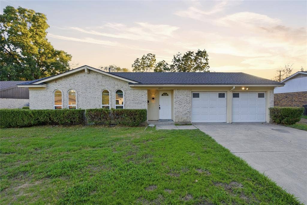 Single-story residence featuring a brick facade, arched window detailing, an attached two-car garage, and a concrete driveway