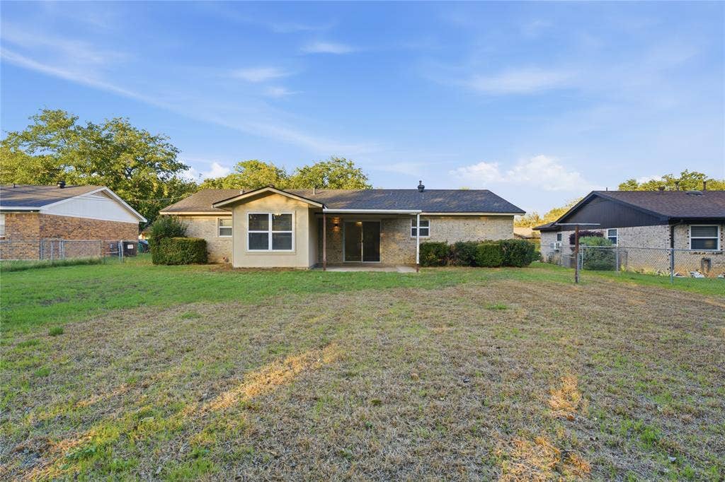 Exterior view featuring a brick facade, covered concrete patio, asphalt shingle roof, and expansive lawn space