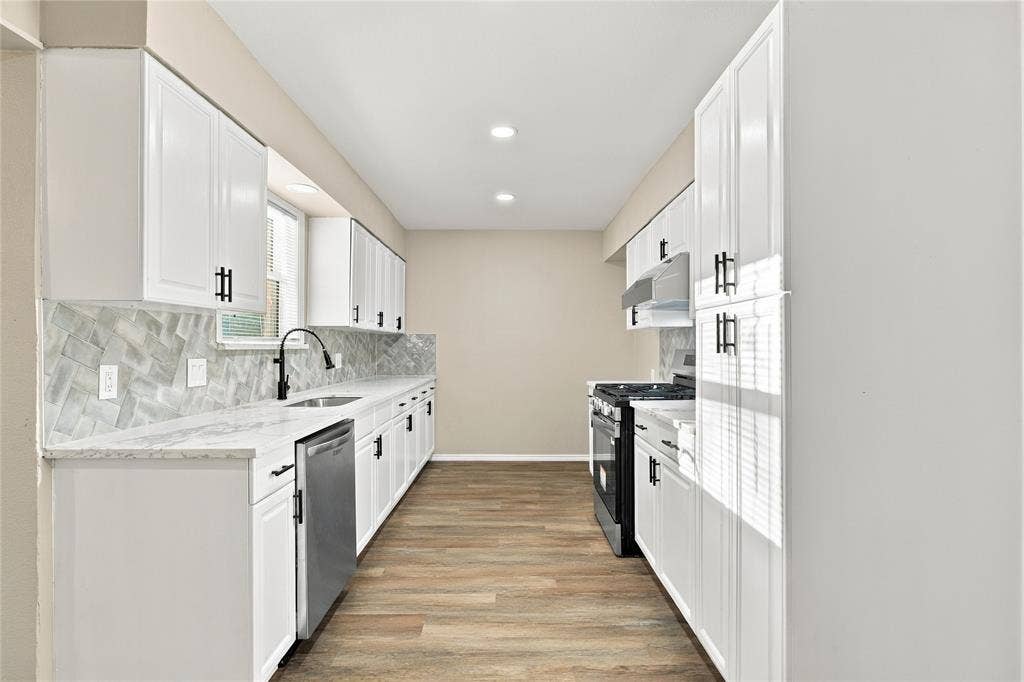 Kitchen featuring white shaker-style cabinetry, herringbone-patterned tile backsplash, light stone-finish countertops, stainless steel appliances, and wood-finish flooring