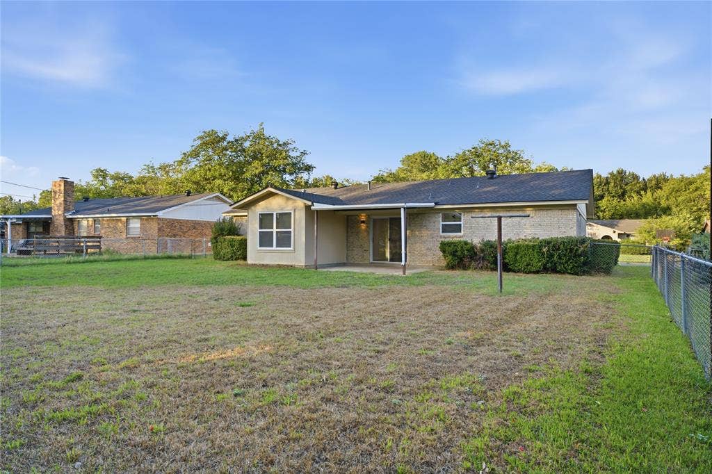 Brick exterior featuring a covered patio, expansive lawn, and perimeter chain-link fencing