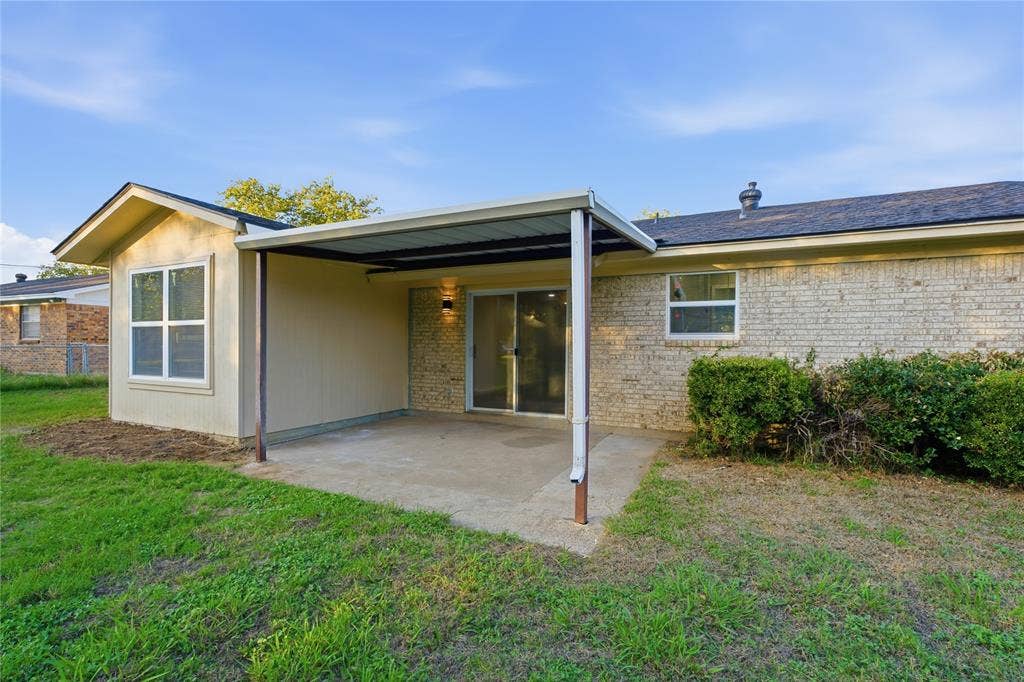 Covered concrete patio with a metal roof extension, brick and siding exterior, and sliding glass door
