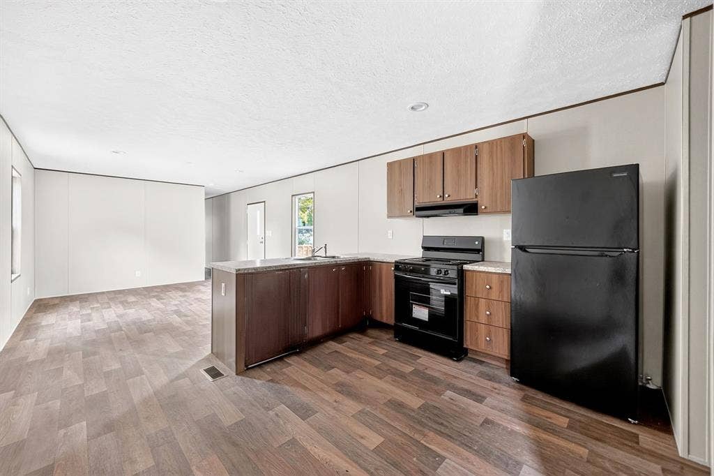 222 W Acres Road, Gun Barrel City, TX 75156 Kitchen featuring wood-finish cabinetry, stone-pattern countertops, and integrated black appliances including a range and refrigerator, complemented by wood-finish flooring