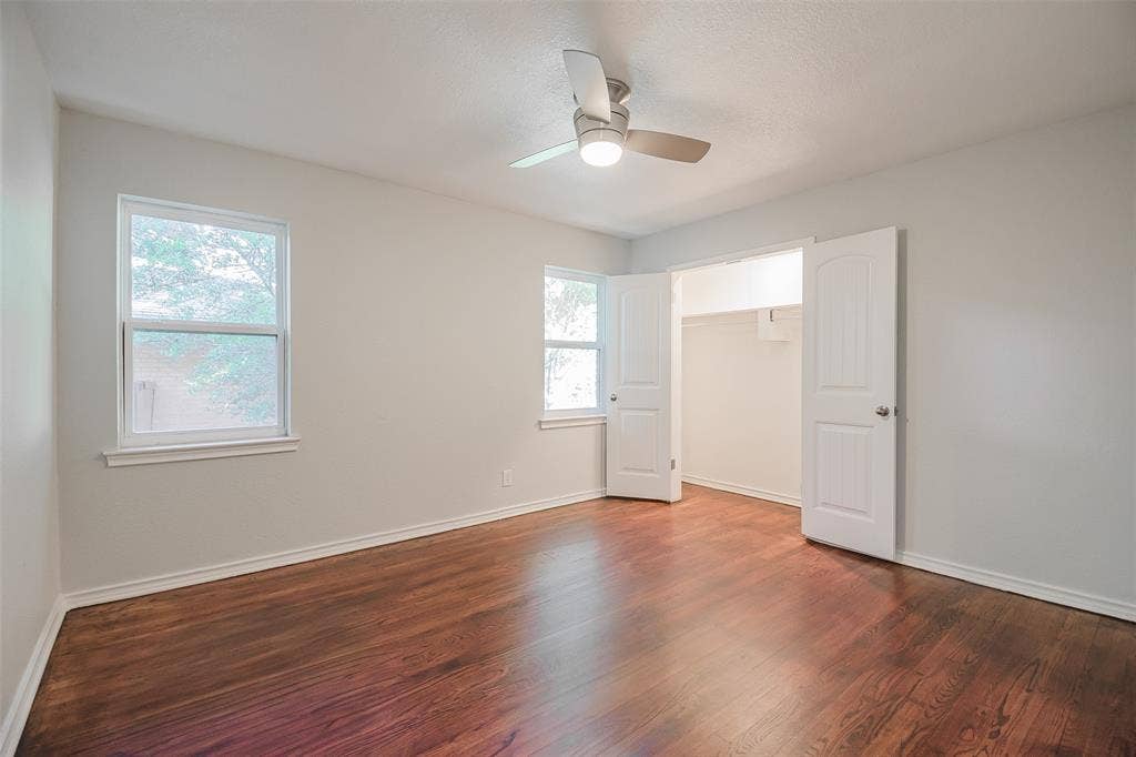 8050 Fall River Drive, Dallas, TX 75228 Room featuring wood-finish flooring, two double-hung windows, a ceiling-mounted light fixture with fan, and a double-door closet