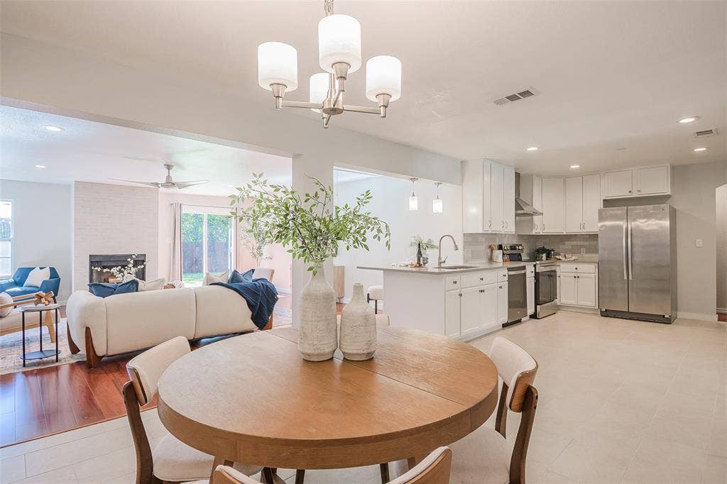 8050 Fall River Drive, Dallas, TX 75228 Open-concept area featuring white cabinetry, stainless steel appliances, kitchen island, recessed lighting, and a fireplace with a light-toned surround