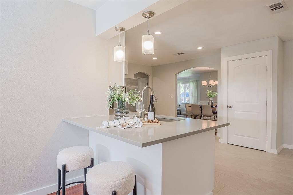 8050 Fall River Drive, Dallas, TX 75228 Kitchen island with solid surface countertop and undermount sink, illuminated by dual hanging pendant lights and featuring an arched architectural opening