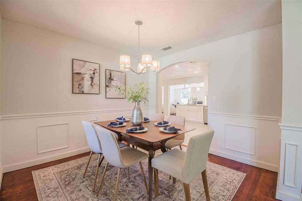 8050 Fall River Drive, Dallas, TX 75228 Dining area featuring wood-finish flooring, wainscoting, and a multi-light chandelier under a high ceiling