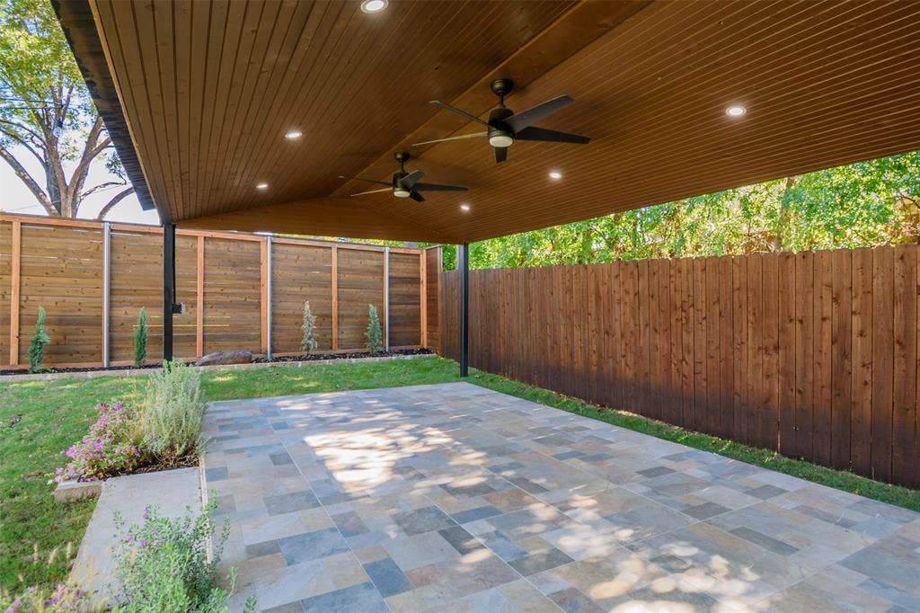 8050 Fall River Drive, Dallas, TX 75228 Covered patio featuring a wood-plank ceiling, recessed lighting, dual ceiling fans, and multi-tonal stone flooring, enclosed by a wood privacy fence