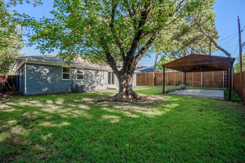 8050 Fall River Drive, Dallas, TX 75228 Backyard featuring a painted brick exterior, large mature tree, covered patio, and full wood perimeter fencing