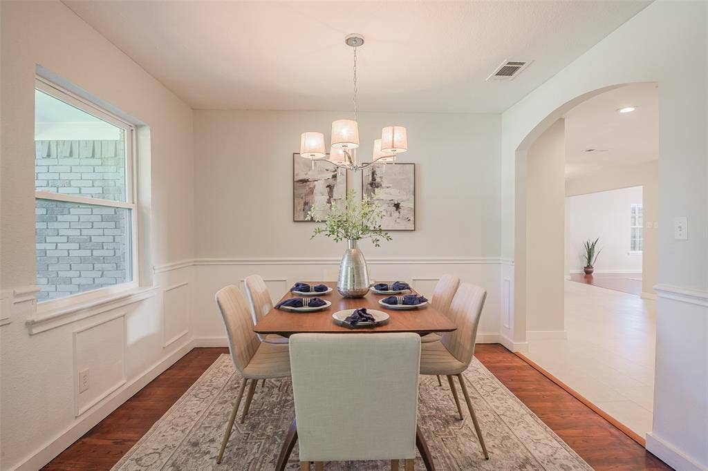 8050 Fall River Drive, Dallas, TX 75228 Dining area featuring wood-finish flooring, white wainscoting, an arched entryway, and a multi-arm drum chandelier