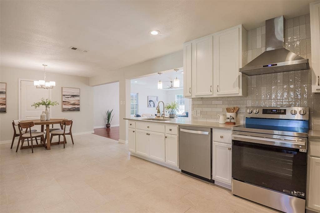 8050 Fall River Drive, Dallas, TX 75228 Kitchen featuring white cabinetry, solid-surface countertops, subway tile backsplash, stainless steel appliances, and a range hood