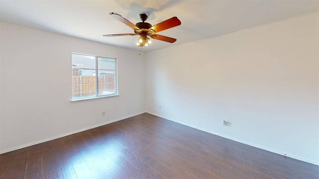 Room featuring wood-finish flooring, a ceiling fan with integrated lighting, and a window with a view of exterior fencing