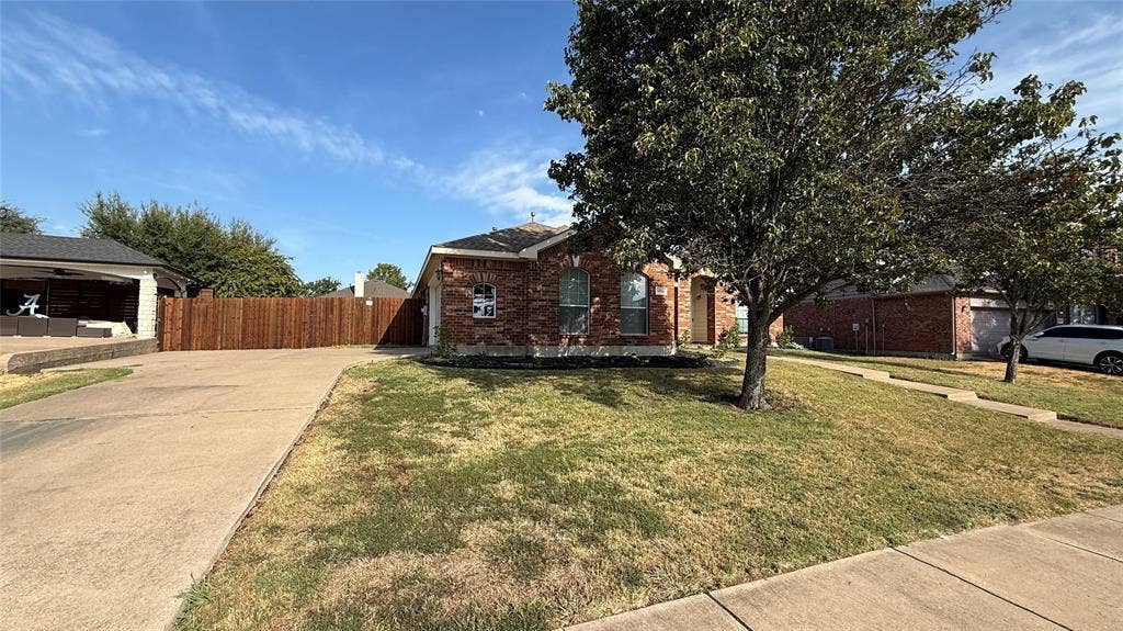 Brick exterior residence featuring a front-facing concrete driveway, arched window detailing, and a privacy wood fence
