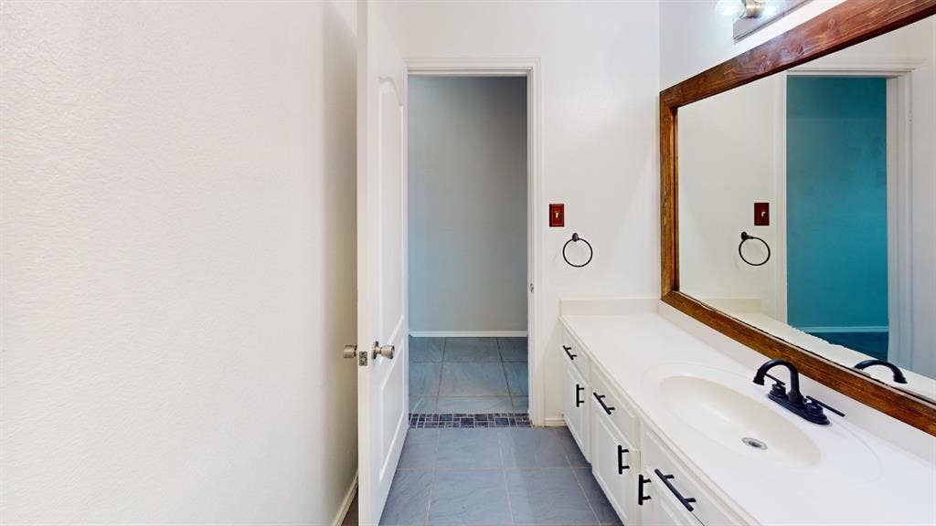 Bathroom vanity featuring white cabinetry, a solid surface countertop with integrated basin, matte black hardware, and a large wood-framed mirror