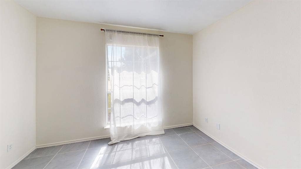 Neutral interior room featuring large-format tile flooring and a single window with a metal curtain rod