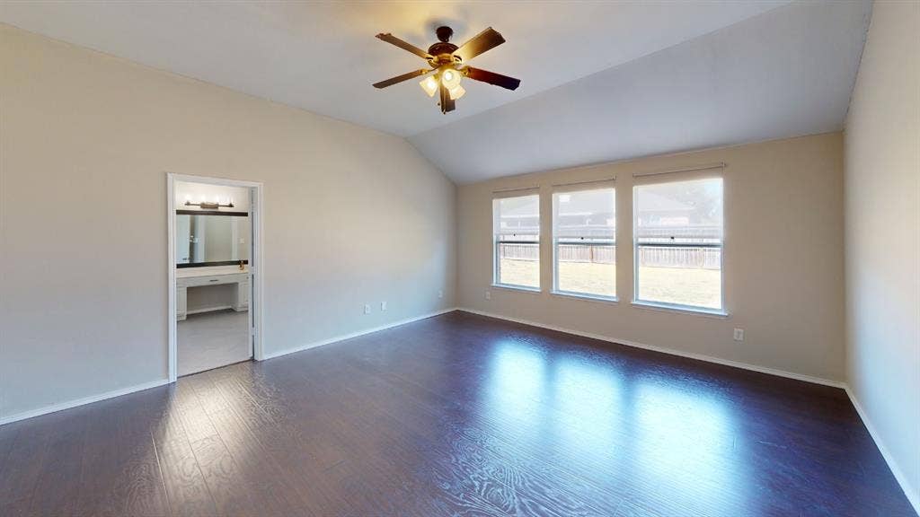 Vaulted ceilings, wood-finish flooring, three large windows, and a ceiling fan with integrated lighting