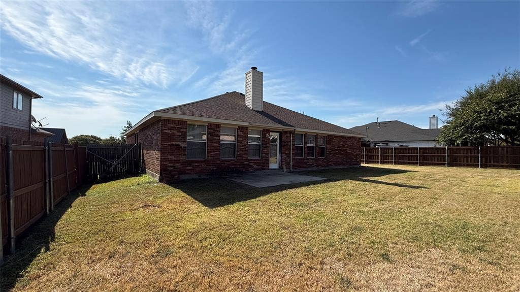Backyard featuring a brick exterior, shingled roof, exterior chimney, concrete patio, and full wood perimeter fencing