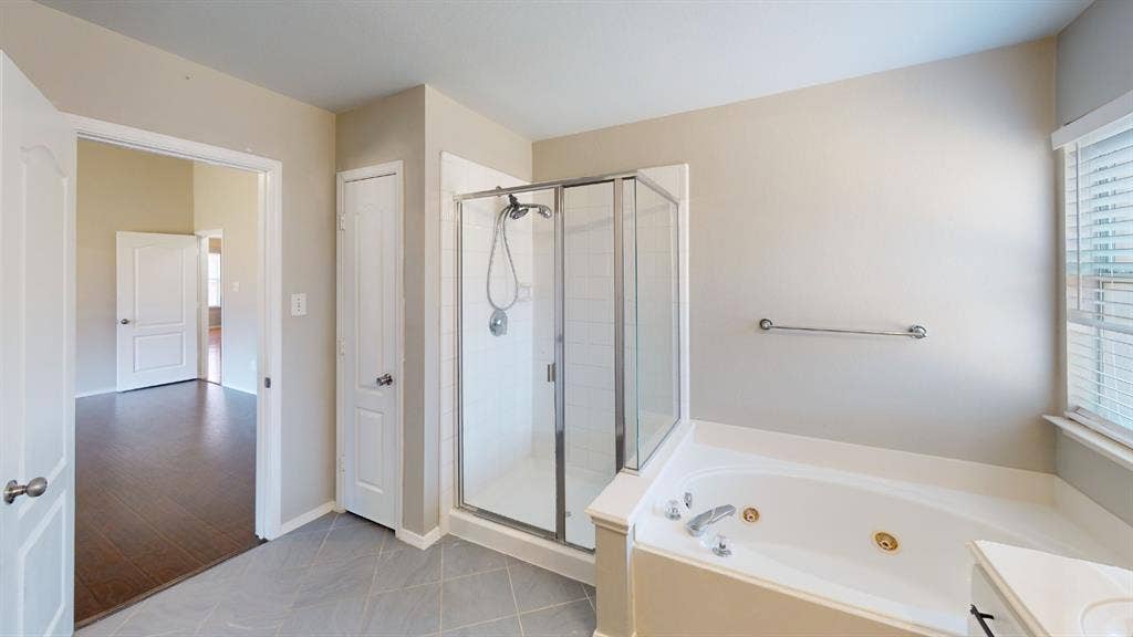 Bathroom featuring a corner jetted soaking tub, glass-enclosed shower with tiled surround, and tile flooring