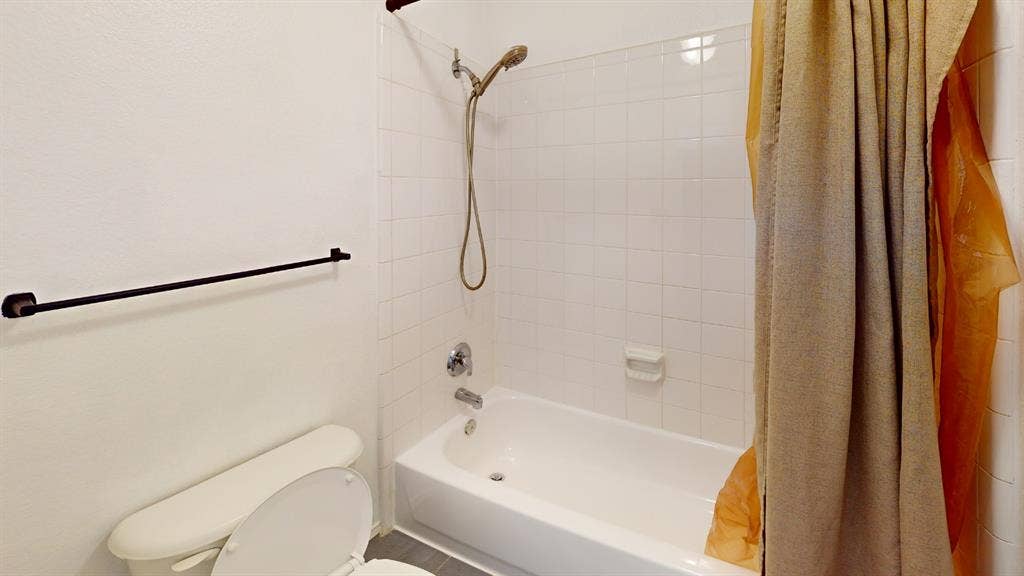 Bathroom featuring a white porcelain tub, ceramic wall tile surround, adjustable handheld shower fixture, and a wall-mounted matte black towel bar