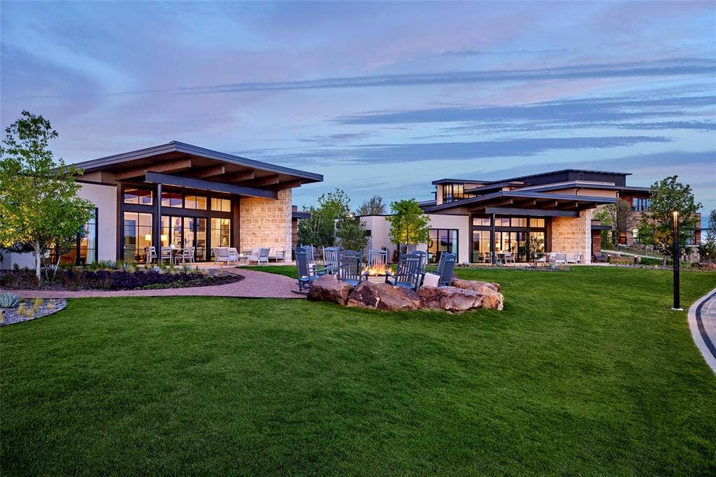 FRISCO PGA Modern architectural exterior featuring expansive glass walls, horizontal rooflines, stone facade accents, and a stone-encased fire pit set within a landscaped lawn